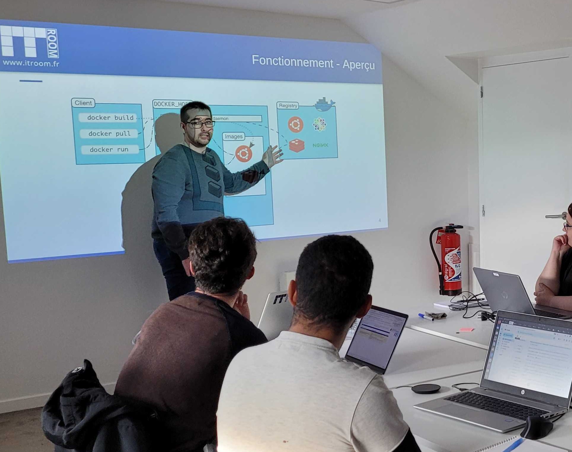 Formateur IT-Room présentant une session technique sur Docker à trois collaborateurs en salle de formation interne